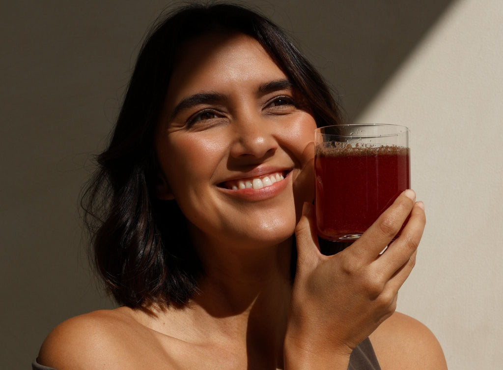 Woman holding a glass of Revitalise Superblend against a neutral background