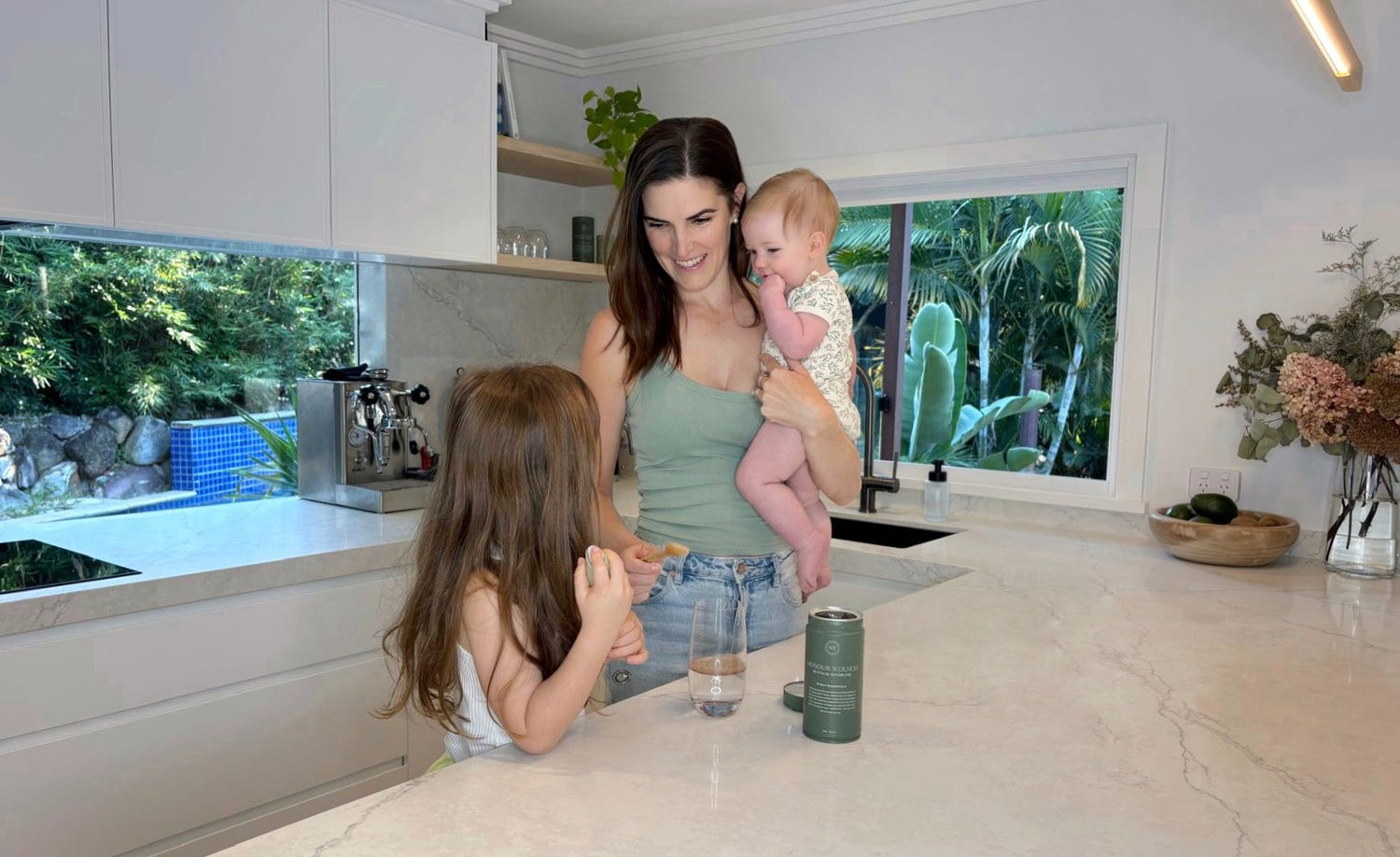 Tahnee, Honour Wellness co-founder, in her kitchen with her two children and a tin of Mothers Replenishment